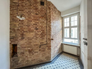 Teil eines Wohnraums mit freigelegter Ziegelwand auf der einen und Fenster auf der anderen Seite.