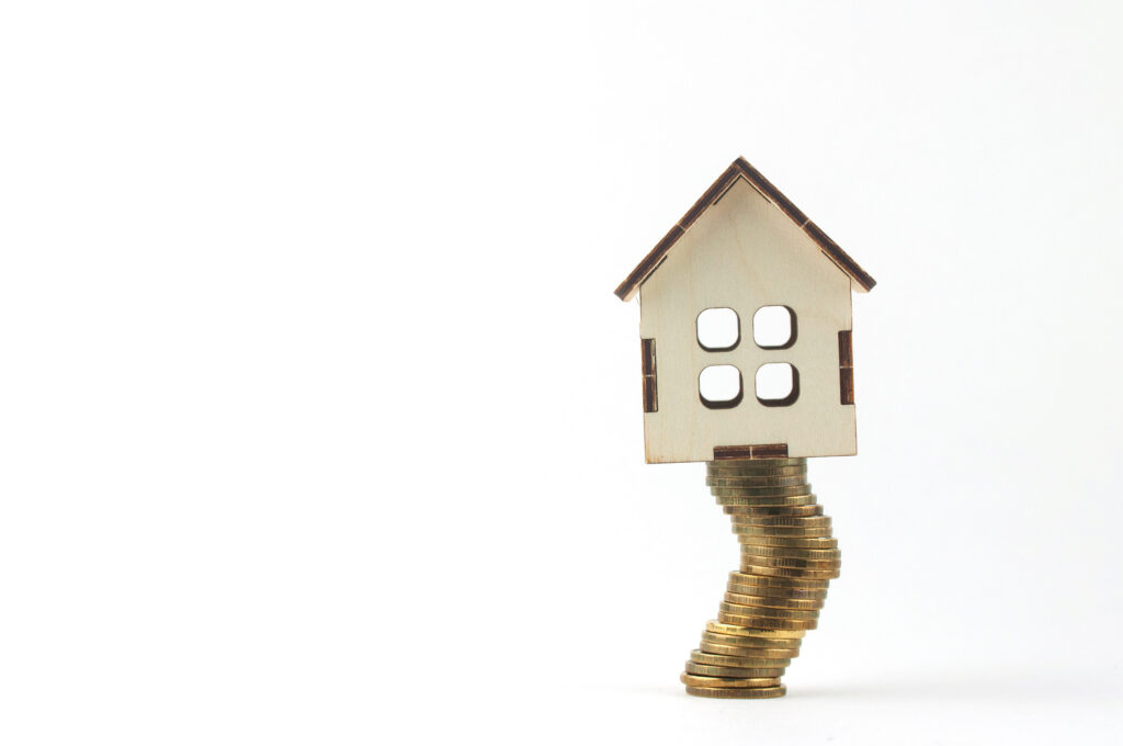 Ein Haus steht auf vielen zu einem Turm gestapelten Geldstücken.